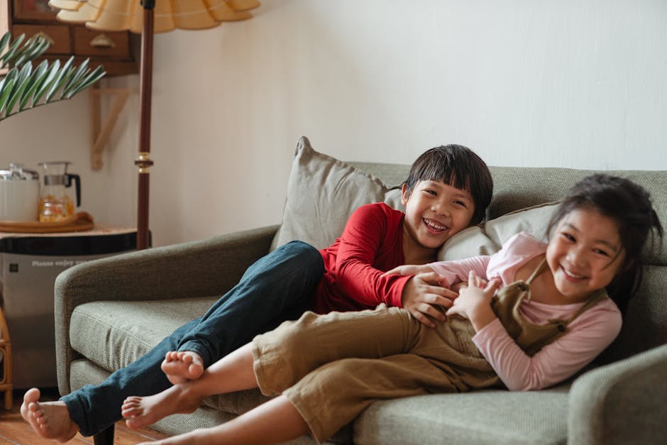 PVHC for Children Two happy children laughing and playing on a couch indoors, showcasing joyful sibling interaction.